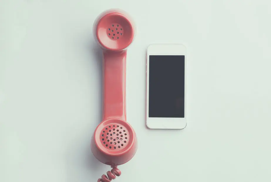 Ein rosa Telefonhörer im Retro-Stil liegt neben einem Smartphone